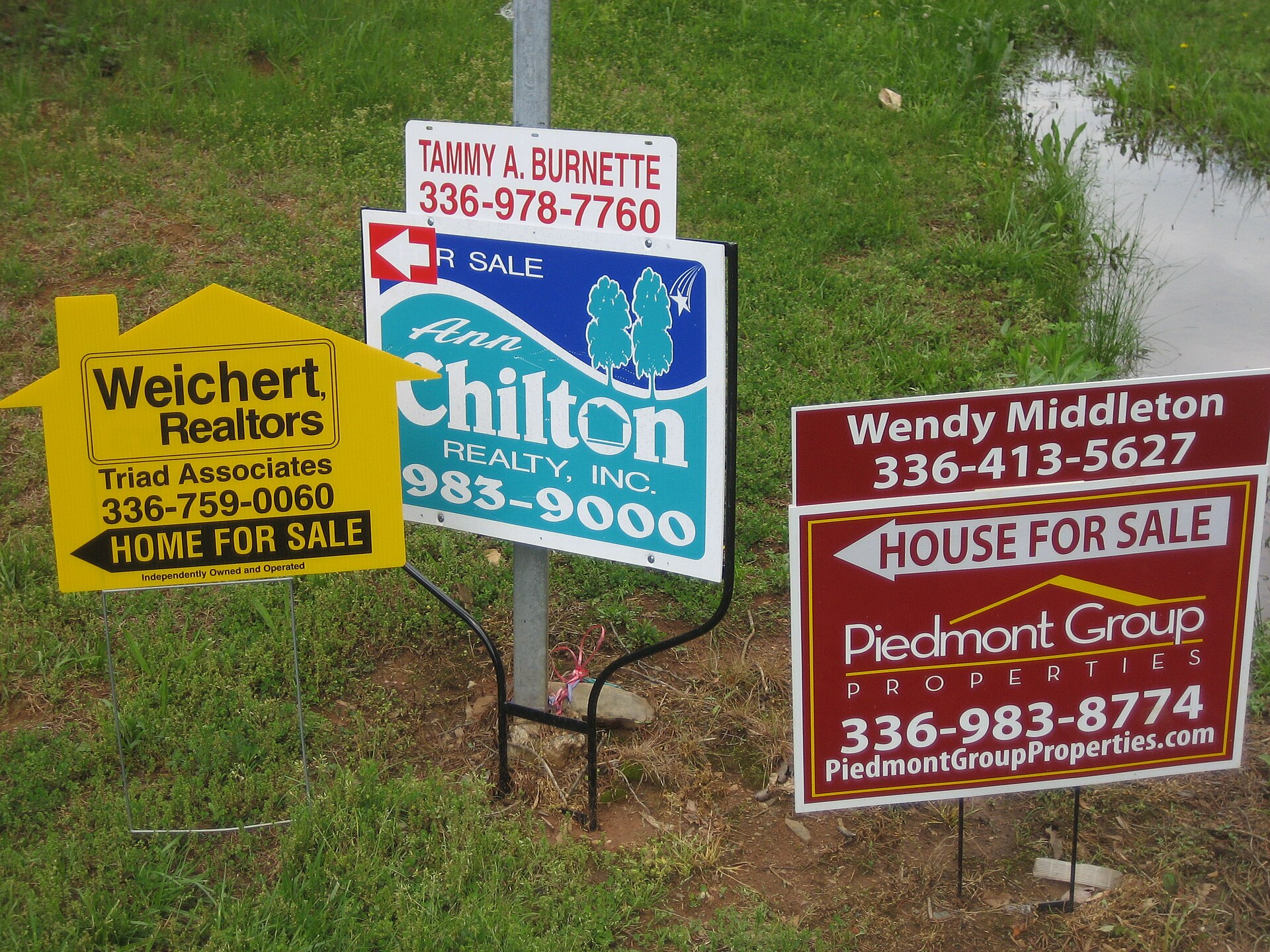 Cluster of real-estate 'House for Sale' signs from multiple realtors — the competitive landlord market Airbnb rental-arbitrage operators navigate to close their first deal.