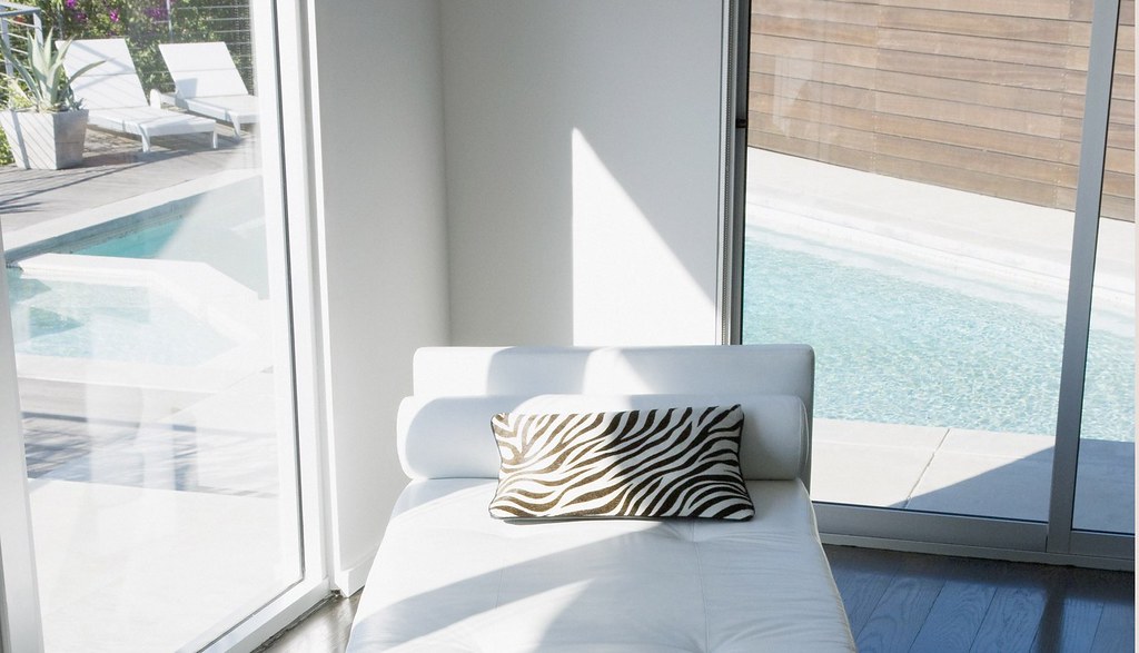 Clean minimalist interior — white chaise lounge, glass walls, single accent pillow — illustrating the disciplined monochromatic approach.